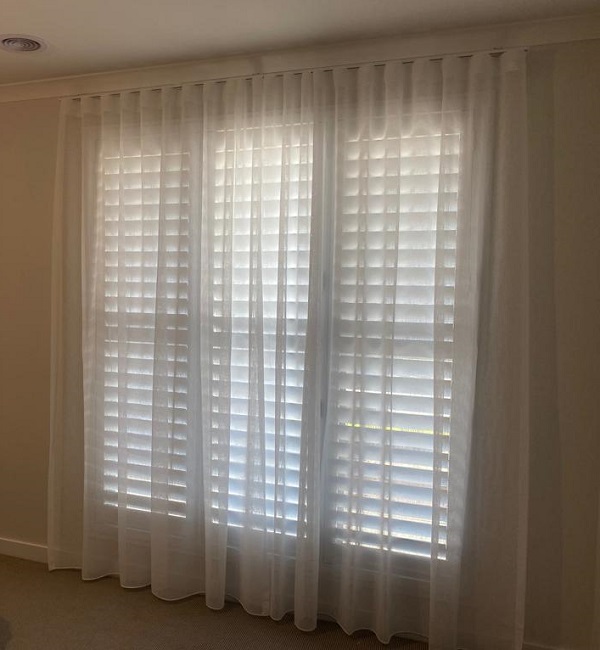 White PVC Plantation Shutters with open slats and a white sheer curtain covering the windows in Glengala 3020 VIC